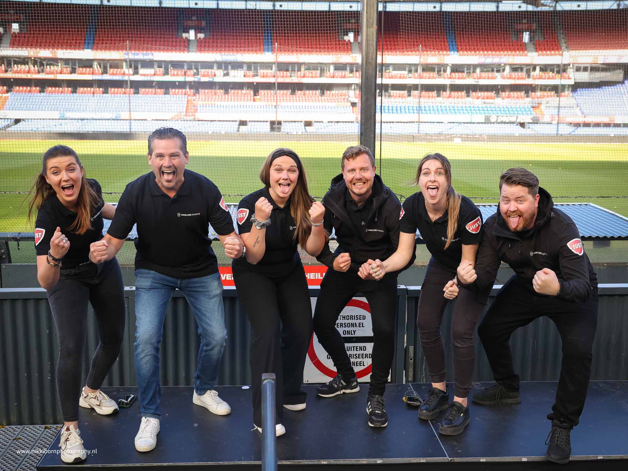 5 medewerkers van timeless events steken hun tong uit en vuisten omhoog met een voetbalveld op de achtergrond - Timeless Events