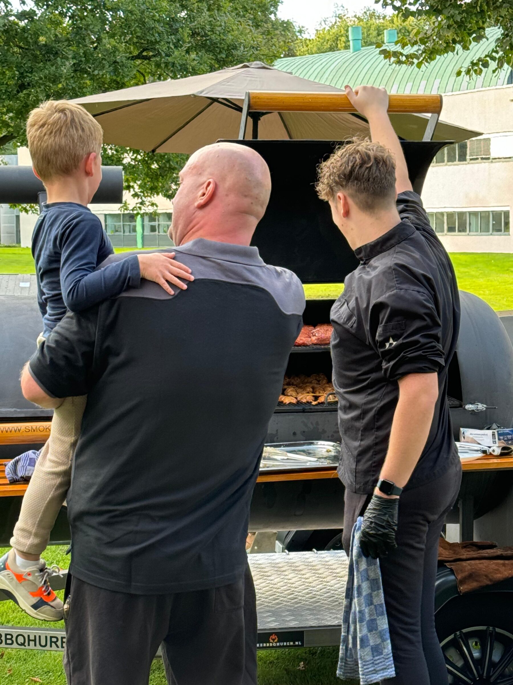 Een man met een kind in zijn armen kijken naar het vlees op de barbecue - Timeless Events