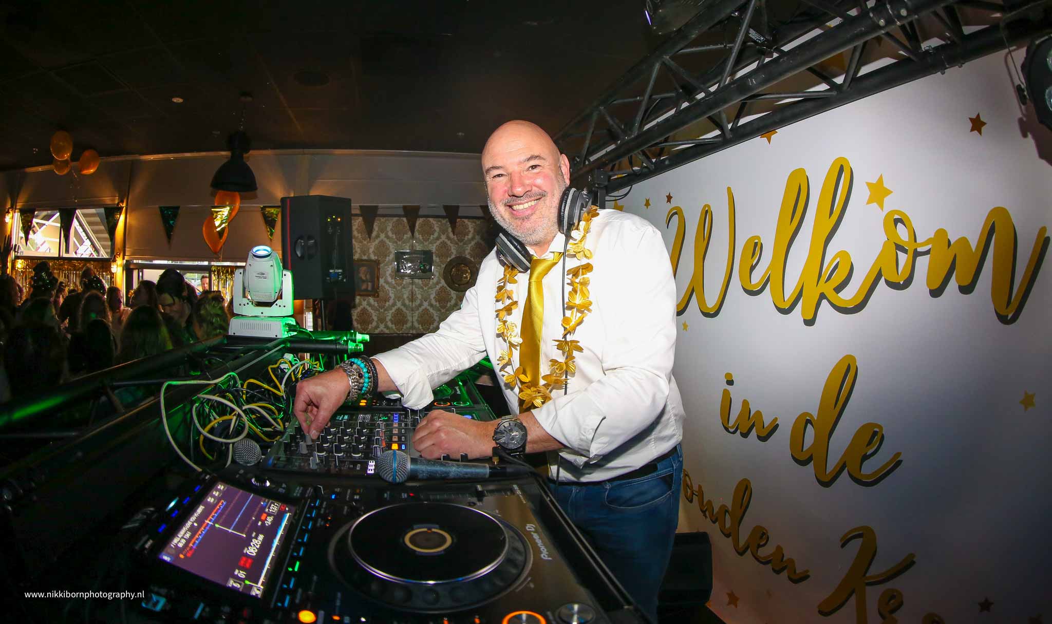 Lachende DJ achter dj-set met gouden bloemenkrans om - Timeless Events