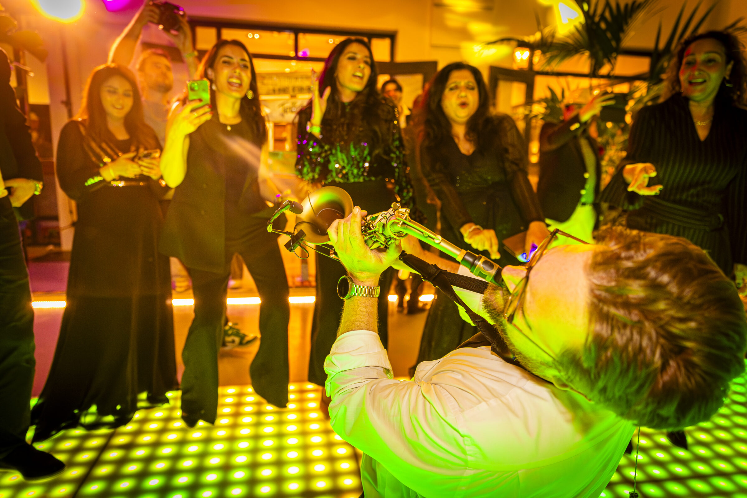 Man op zijn knie&euml;n die saxofoon speelt met een groep vrouwen eromheen - Timeless Events