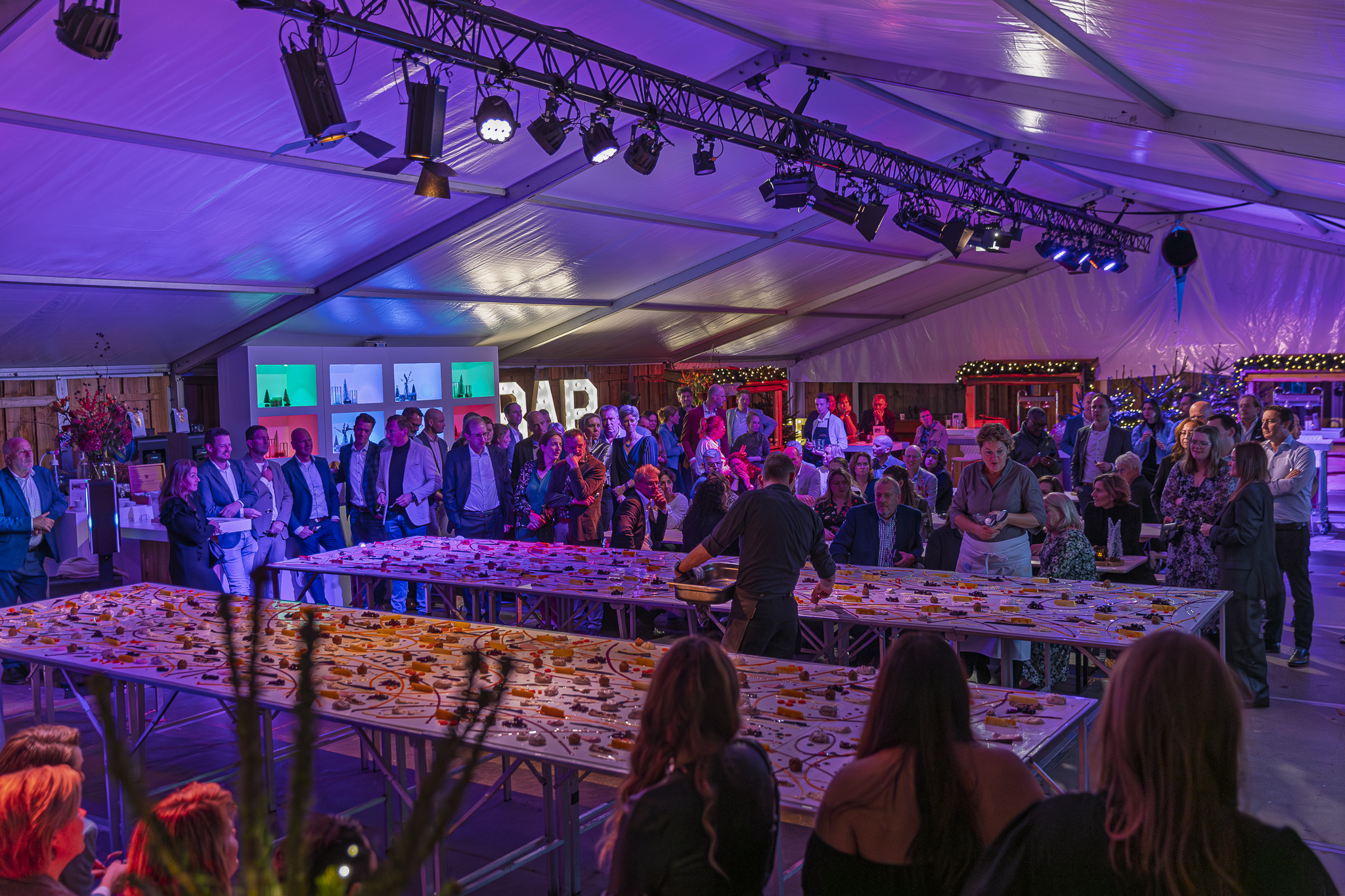 Uitzicht op de tafels vol met hapjes en een groep mensen eromheen - Timeless Events