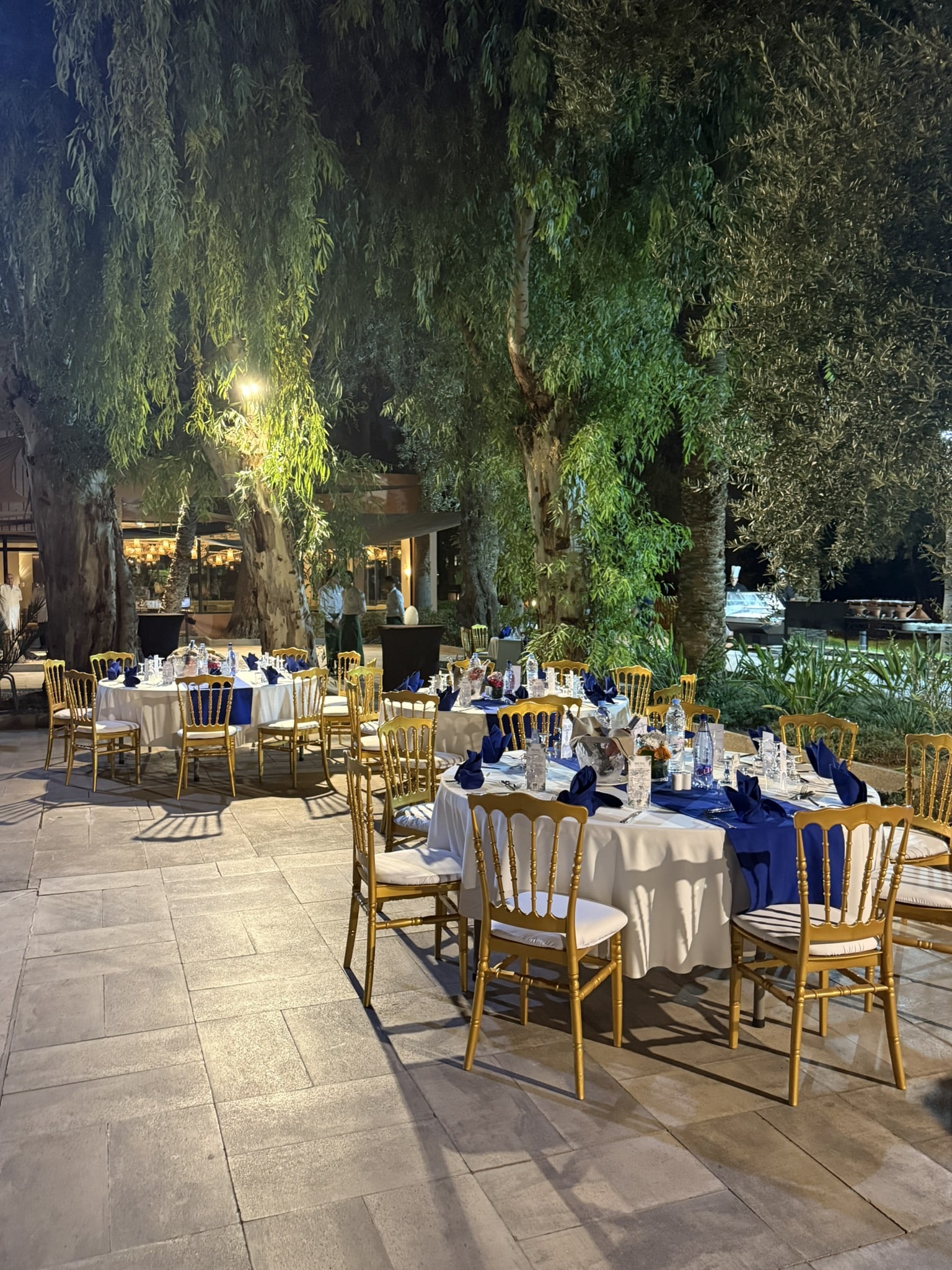 gedekte ronde tafels met gouden stoelen op buitenterrein in de avond